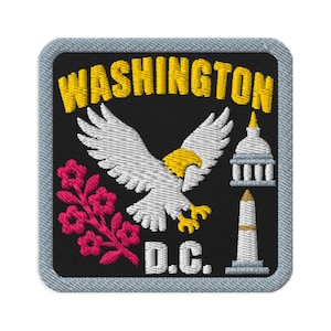 Könnte beinhalten: Ein quadratischer gestickter Aufnäher mit schwarzem Hintergrund und hellblauem Rand. Er zeigt den gelben Schriftzug WASHINGTON über einem weißen Adler mit gelbem Kopf und gelben Füßen, einem rosa Kirschblütenzweig, dem weißen Text D.C. und weißen Monumenten.