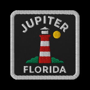 Peut inclure: Écusson brodé avec un phare à rayures rouges et blanches, un soleil jaune et le texte "JUPITER FLORIDA" en blanc. Le patch a un fond noir et une bordure blanche.