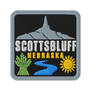 Peut inclure: Un écusson brodé carré avec un fond noir et une bordure grise. Il présente une silhouette de montagne grise, le texte blanc SCOTTSBLUFF, le texte jaune NEBRASKA, une gerbe de blé verte, une rivière bleue sinueuse et un soleil jaune.
