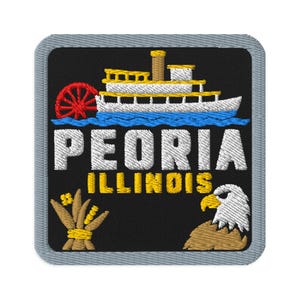 Op de afbeelding: Een vierkante geborduurde patch met een grijze rand op een zwarte achtergrond. Het toont een wit en geel stoomschip met een rood schoepenrad, de tekst PEORIA ILLINOIS in wit en geel, een beige korenschoof en een witte Amerikaanse zeearendkop.