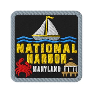 May include: A square embroidered patch with a black background and a grey border. It features a white sailboat with a yellow mast, blue waves, a red crab, and a tan gazebo. The text reads NATIONAL HARBOR in yellow and MARYLAND in white.
