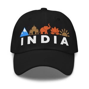 May include: A black baseball cap featuring the word INDIA in white capital letters. Above the text are five colourful icons: a blue mountain, a tan building, an orange elephant, an orange lotus flower, and a tan sun rising over a horizon.