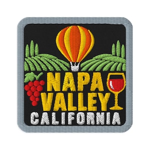 Peut inclure: Un écusson brodé carré sur fond noir représentant une montgolfière jaune et orange au-dessus de collines de vignobles vertes. Le texte NAPA VALLEY CALIFORNIA est brodé en jaune et blanc, avec une grappe de raisin rouge et un verre de vin.