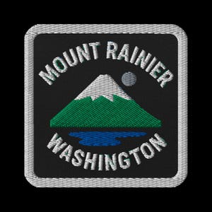 Puede incluir: Parche bordado con el Monte Rainier en el estado de Washington. El diseño incluye una montaña de pico blanco, colinas verdes, agua azul y una luna gris sobre un fondo negro. Las palabras "Mount Rainier" y "Washington" están bordadas en blanco.