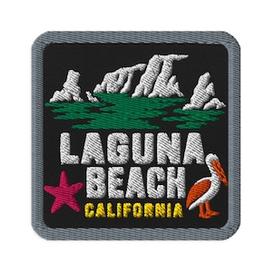May include: A square embroidered patch with a black background and a grey border. It features white mountain peaks above green water, a pink starfish, an orange and white pelican, and the white text LAGUNA BEACH with yellow CALIFORNIA text.