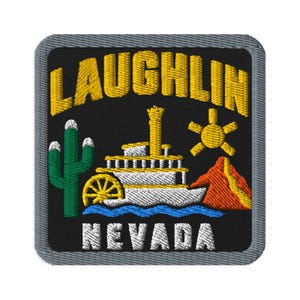 May include: A square embroidered patch with a black background and a grey border. It features the yellow text LAUGHLIN at the top and NEVADA at the bottom. The design includes a white paddlewheel boat, a green cactus, a yellow sun, and a red mountain.