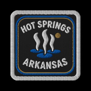 May include: Embroidered patch featuring the text "HOT SPRINGS ARKANSAS" in white, arched over and under a graphic of three stylized steam plumes and a sun. The patch has a black background with blue and gold borders, and a white stitched edge.