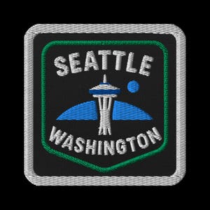 May include: Embroidered patch featuring the Seattle Space Needle, a blue circle, and blue wings. The words "SEATTLE WASHINGTON" are in white, arched around the Space Needle. The patch has a black background, green border, and silver trim.