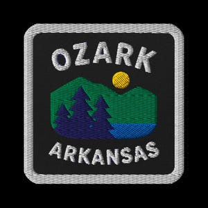 May include: Embroidered patch featuring the text "OZARK ARKANSAS" in white, arched over a landscape scene. The scene includes green and blue mountains, a yellow sun, and dark blue trees. The patch has a black background and a white border.