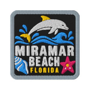 May include: A square embroidered patch with a black background and a gray border. It features a gray dolphin leaping over blue waves, a blue seashell, a pink starfish, and the white text MIRAMAR BEACH with yellow text FLORIDA below it.