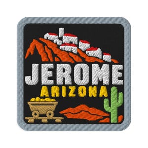 Puede incluir: Un parche bordado cuadrado con borde gris sobre fondo negro. Presenta un pueblo en la ladera en blanco y rojo, el texto JEROME ARIZONA en blanco y amarillo, una vagoneta minera color canela llena de oro y un cactus saguaro verde sobre colinas naranjas.