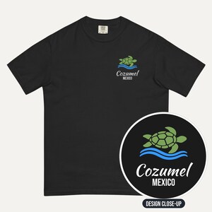 May include: A black short-sleeve t-shirt featuring a small graphic on the left chest of a green sea turtle swimming above blue waves, with the text Cozumel MEXICO printed below in white and script lettering.