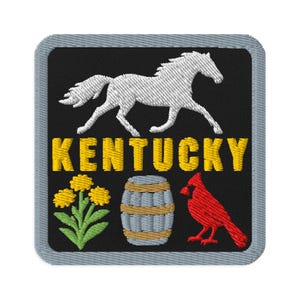 May include: A square embroidered patch with a grey border on a black background. It features a white horse, the yellow text KENTUCKY, a cluster of yellow flowers with green stems, a grey and tan barrel, and a red cardinal bird facing left.
