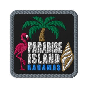 May include: A square embroidered patch with a black background and a gray border. It features a green palm tree, a pink flamingo, and a tan seashell. The white text reads PARADISE ISLAND, with the blue text BAHAMAS underneath the white text.