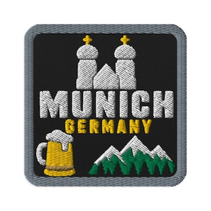 May include: A square embroidered patch with a black background and a gray border. It features a white illustration of the Munich Frauenkirche, the text MUNICH in white, GERMANY in yellow, a yellow beer mug with white foam, and green mountains.