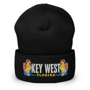 Può includere: Un berretto nero con risvolto caratterizzato da un ricamo sul davanti. Il testo riporta KEY WEST in bianco e FLORIDA in giallo. Due galli colorati con corpo giallo, cresta rossa e piume della coda blu fiancheggiano il testo su entrambi i lati.