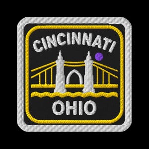 May include: Embroidered patch featuring the city name "Cincinnati" and "Ohio" in white, with a yellow and white border. The design includes a bridge and a purple dot on a black background.