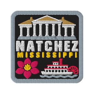 Puede incluir: Un parche bordado cuadrado con borde gris sobre fondo negro. Presenta un edificio neoclásico blanco, el texto NATCHEZ en blanco, MISSISSIPPI en amarillo, una flor rosa con centro amarillo y un barco de vapor de ruedas blanco y rojo.