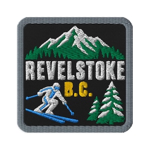 May include: A square embroidered patch with a black background featuring a white snow-capped mountain range above green pine trees. The text REVELSTOKE B.C. is in white and yellow. A white skier with blue accents is on the left, and two pine trees are on the right.