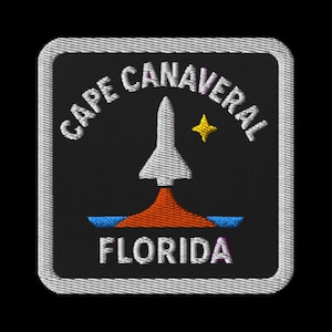 May include: Embroidered patch featuring "CAPE CANAVERAL FLORIDA" in white text. A white rocket launches from an orange flame, with a yellow star above. Blue lines represent water. The patch has a black background and a white border.