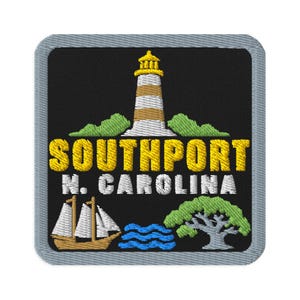 Puede incluir: Un parche bordado cuadrado con fondo negro y borde gris. Presenta un faro, un velero, un árbol y olas azules. El texto SOUTHPORT N. CAROLINA está bordado con hilo amarillo y blanco sobre la tela negra del parche.