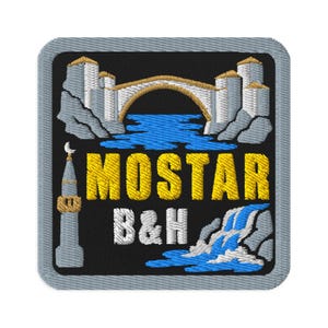 Peut inclure: Un écusson brodé carré sur fond noir représentant un pont en pierre gris clair au-dessus d'une eau bleue, un minaret gris avec un croissant de lune et une cascade. Le texte MOSTAR est en jaune et B&H en blanc, le tout bordé de gris.