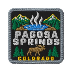 May include: A square embroidered patch with a black background and a gray border. It features a blue hot spring with white steam, green pine trees, snow-capped mountains, a brown elk, and the text PAGOSA SPRINGS COLORADO in white and yellow.