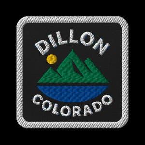Puede incluir: Parche bordado con el texto "DILLON COLORADO" en blanco, encima y debajo de una cordillera verde y un lago azul. Un sol amarillo está posicionado a la izquierda de las montañas. El parche tiene un fondo negro y un borde blanco.