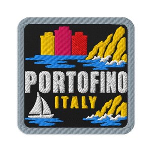 Puede incluir: Un parche bordado cuadrado con fondo negro que muestra un horizonte de edificios amarillos, rosas y rojos sobre agua azul. El texto PORTOFINO ITALY está bordado en blanco y amarillo. También se ven un velero blanco y acantilados amarillos.