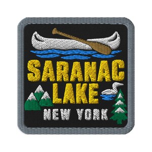 Peut inclure: Un écusson brodé carré avec une bordure grise sur fond noir. Il présente un canoë blanc avec une pagaie marron sur une eau bleue, le texte jaune SARANAC LAKE, le texte blanc NEW YORK, des montagnes vertes et un sapin vert.