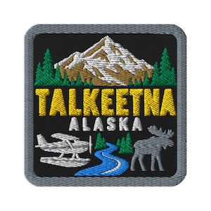Può includere: Una toppa ricamata quadrata con sfondo nero raffigurante una montagna innevata, pini verdi e il testo giallo TALKEETNA sopra il testo bianco ALASKA. In basso sono presenti un idrovolante bianco, un fiume blu e la sagoma di un alce grigio.