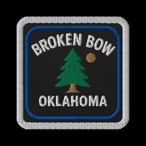 May include: Embroidered patch featuring the text "BROKEN BOW OKLAHOMA" in white, arched over a green tree and a gold circle on a black background. The patch has a blue border and a white stitched edge.