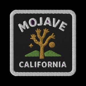 Può includere: Toppa ricamata con la scritta "MOJAVE CALIFORNIA" in bianco, un disegno di albero di Giosuè dorato, una stella, un sole e colline verdi su sfondo nero. La toppa ha un bordo bianco.