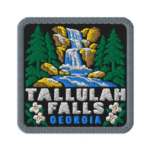 May include: A square embroidered patch with a black background featuring a waterfall cascading over tan rocks, flanked by green pine trees. Below the waterfall, white text reads TALLULAH FALLS and blue text reads GEORGIA, with small white flowers.