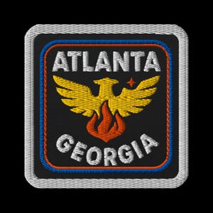 May include: Embroidered patch featuring the words "ATLANTA GEORGIA" in white, with a gold phoenix rising above flames. The patch has a black background, a blue and orange border, and a white stitched edge.