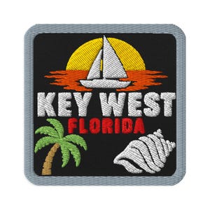 May include: A square embroidered patch with a black background and a gray border. It features a white sailboat on orange water against a yellow sun, the white text KEY WEST, red text FLORIDA, a green palm tree, and a white seashell graphic.