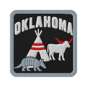 Puede incluir: Un parche bordado cuadrado con fondo negro y borde gris claro. El texto OKLAHOMA está arqueado en blanco en la parte superior. Debajo, un tipi blanco con rayas rojas, un buey longhorn blanco con cuernos rojos y un armadillo gris.