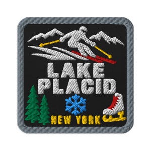 Puede incluir: Un parche bordado cuadrado con fondo negro y borde gris. Presenta un esquiador blanco sobre una montaña, el texto LAKE PLACID en blanco, dos pinos verdes, un copo de nieve azul, un patín de hielo blanco y el texto NEW YORK en amarillo.