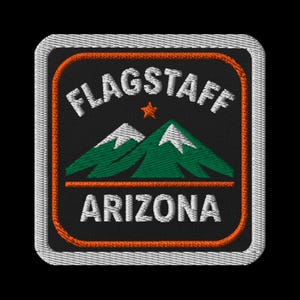 May include: Embroidered patch featuring the text "FLAGSTAFF ARIZONA" in white, with a small orange star and green mountain range graphic. The patch has an orange border and a white stitched edge, set against a black background.