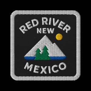 May include: Embroidered patch featuring the text "RED RIVER NEW MEXICO" in white, arched over a mountain scene. The design includes a white mountain, green trees, a yellow sun, and a blue river, all on a black background.