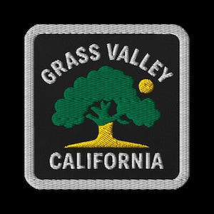 May include: Embroidered patch featuring the text "GRASS VALLEY CALIFORNIA" in white, arched over and under a green tree with a yellow trunk and a yellow sun. The patch has a black background and a silver border.