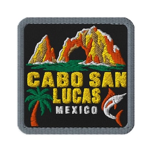 Op de afbeelding: Een vierkante geborduurde patch met een zwarte achtergrond met een geel, oranje en wit rotsboogformatie boven groen water. De tekst CABO SAN LUCAS MEXICO is in het geel en wit, met een groene palmboom en een springende oranje vis.