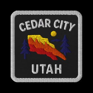 Peut inclure: Écusson brodé avec le texte "CEDAR CITY UTAH" en blanc. Le motif comprend une chaîne de montagnes stylisée en jaune, orange et rouge, un soleil jaune et deux pins bleus sur fond noir, avec une bordure blanche.