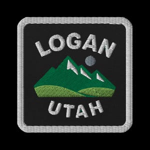 Peut inclure: Écusson brodé avec le texte "LOGAN UTAH" en blanc, au-dessus et en dessous d'une chaîne de montagnes vertes avec des sommets enneigés blancs. Un petit cercle gris est au-dessus des montagnes. L'écusson a un fond noir et une bordure blanche.