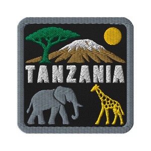 Puede incluir: Un parche bordado cuadrado con fondo negro que presenta un árbol de acacia verde, una montaña marrón con una cima nevada blanca y un sol amarillo. La palabra TANZANIA está bordada en letras blancas sobre un elefante gris y una jirafa amarilla.