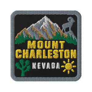 May include: A square embroidered patch with a black background featuring a mountain range, a bighorn sheep, green pine trees, a green cactus, and a yellow sun. The text reads MOUNT CHARLESTON in yellow and NEVADA in white with a grey border.