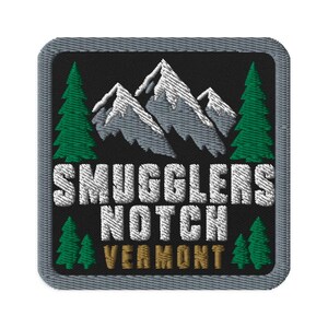 May include: A square embroidered patch with a black background and a gray border. It features a white and gray mountain range, green pine trees, and the white text SMUGGLERS NOTCH with the brown text VERMONT centered below the mountain graphic.