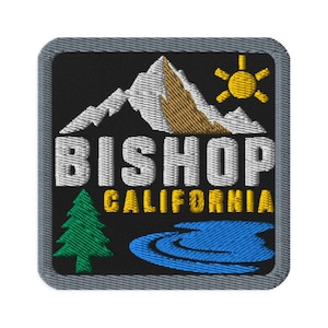 May include: A square embroidered patch with a black background featuring a white and brown mountain range, a yellow sun, a green pine tree, and a blue lake. The text BISHOP is embroidered in white, and CALIFORNIA is embroidered in yellow.
