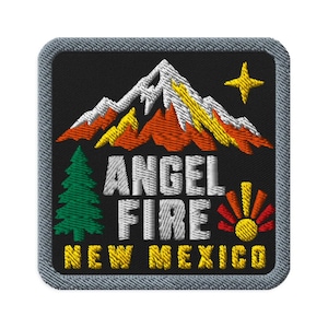May include: A square embroidered patch with a black background and a gray border. It features a mountain range in white, yellow, and orange, a green pine tree, a yellow star, and a yellow sun. The text reads ANGEL FIRE NEW MEXICO in white and yellow.