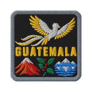 May include: A square embroidered patch with a gray border on a black background. It features a white and yellow bird in flight above the yellow text GUATEMALA. Below the text is a red volcano, a green leafy branch with red berries, and a blue mountain.